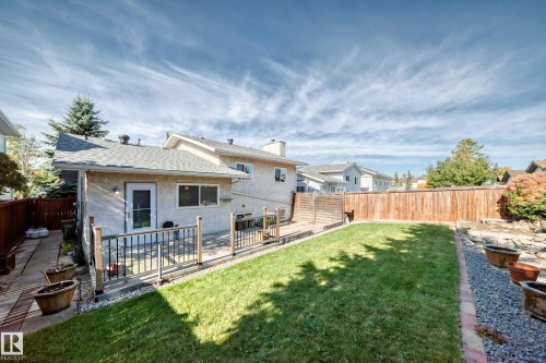 Backyard featuring a wood deck with black metal railings, a manicured lawn, a gravel border, and a wood privacy fence - 14519 32 Street Nw, Edmonton, AB 