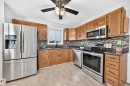 Modern kitchen featuring wood cabinetry, stainless steel appliances including a French-door refrigerator and convection range, mosaic tile backsplash, dark countertops, and brushed nickel hardware throughout - 14519 32 Street Nw, Edmonton, AB 