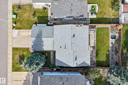 Shingle roof property with an expansive concrete driveway, a front lawn with mature trees, and a rear deck leading to a manicured lawn and a small water feature - 14519 32 Street Nw, Edmonton, AB 