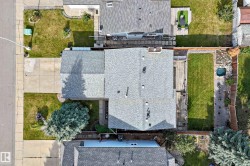 Shingle roof property with an expansive concrete driveway, a front lawn with mature trees, and a rear deck leading to a manicured lawn and a small water feature - 