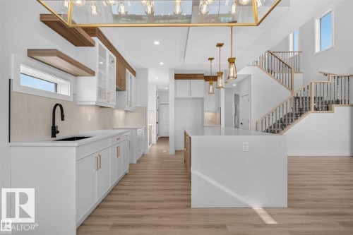 Kitchen featuring white cabinetry, a large kitchen island with a light-toned countertop, and wood-finish flooring - 101 Rosa Crescent, St. Albert, AB 