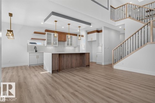 Open-concept living space with wood-finish flooring, a two-story ceiling, and a modern kitchen featuring an island with a breakfast bar - 101 Rosa Crescent, St. Albert, AB 