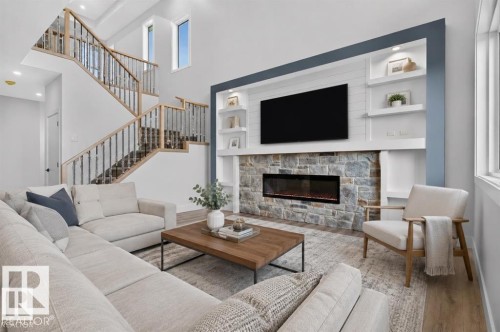 Stone-clad fireplace with built-in electric insert, custom shelving with integrated lighting, two-story ceiling, light wood-finish flooring, and a multi-level staircase with metal balusters - 101 Rosa Crescent, St. Albert, AB 