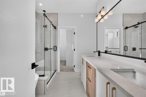 Dual vanity with stone countertop, wood-finish cabinetry, and matte black fixtures - 101 Rosa Crescent, St. Albert, AB 