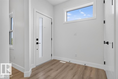Entryway featuring wood-finish flooring, a white front door with vertical glass insert, matte black hardware, and a high horizontal window - 101 Rosa Crescent, St. Albert, AB 