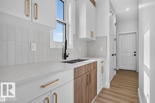 Contemporary kitchen featuring white cabinetry, gold-finish hardware, a matte black faucet, and wood-finish lower cabinetry - 101 Rosa Crescent, St. Albert, AB 