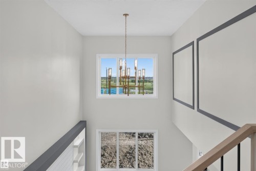 Two-story ceiling with a multi-light chandelier, upper-level rectangular window, lower-level rectangular window, and a wood handrail with metal balusters - 101 Rosa Crescent, St. Albert, AB 