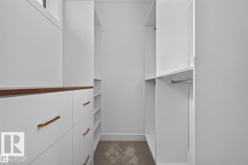 Custom closet system featuring white cabinetry, brass-finish hardware, wood-finish countertop, built-in shelving, and hanging rods - 101 Rosa Crescent, St. Albert, AB 