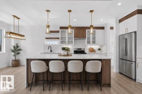 Kitchen featuring a large island with seating, a stainless steel refrigerator, a tile backsplash, and wood-finish flooring - 101 Rosa Crescent, St. Albert, AB 