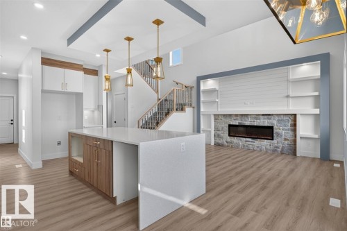 Waterfall island with a quartz countertop, wood-finish flooring, built-in shelving, stone-faced fireplace, and recessed lighting - 101 Rosa Crescent, St. Albert, AB 