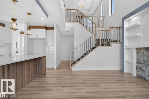 Open-concept living area featuring wood-finish flooring, a contemporary staircase with metal balusters, and a built-in fireplace with a stone surround - 101 Rosa Crescent, St. Albert, AB 