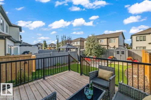 Wood-finish deck with black metal railing, leading to a landscaped yard with artificial turf and a storage shed - 75 Garneau Gate, Spruce Grove, AB 