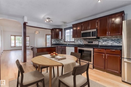 Kitchen featuring dark wood cabinetry, stainless steel appliances, mosaic tile backsplash, and light wood-finish flooring - 18739 72 Avenue Nw, Edmonton, AB 