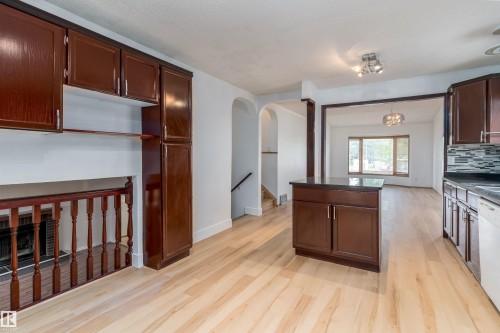 Kitchen featuring wood-finish flooring, dark wood cabinetry, a central island with a dark countertop, and a tiled backsplash - 18739 72 Avenue Nw, Edmonton, AB 