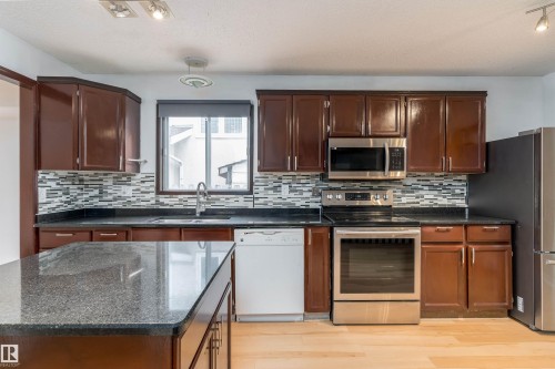 Kitchen featuring dark wood cabinetry, stainless steel appliances, dark stone countertops, and a tiled backsplash - 18739 72 Avenue Nw, Edmonton, AB 