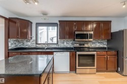 Kitchen featuring dark wood cabinetry, stainless steel appliances, dark stone countertops, and a tiled backsplash - 