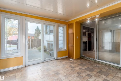 Sunroom featuring multiple windows, sliding glass doors, built-in storage, track lighting, and a durable tile-patterned floor - 18739 72 Avenue Nw, Edmonton, AB 