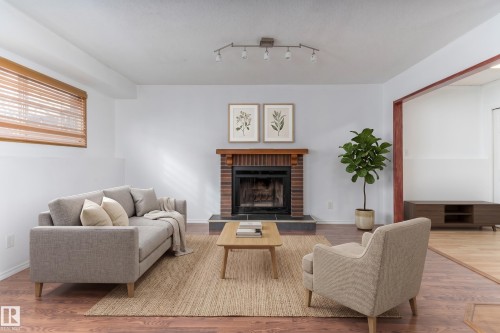 Brick fireplace with wood mantel, track lighting fixture, wood-finish flooring, and window with wood blinds - 18739 72 Avenue Nw, Edmonton, AB 