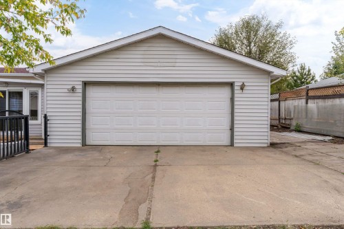 Attached two-car garage with a panel garage door, exterior wall lights, vinyl siding, and a concrete driveway - 18739 72 Avenue Nw, Edmonton, AB 
