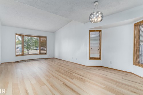 Vaulted ceiling, light wood-finish flooring, bay window, multiple windows with natural wood trim, and a modern ceiling fixture - 18739 72 Avenue Nw, Edmonton, AB 