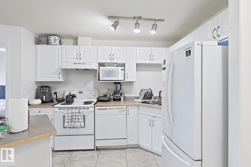 White cabinetry with overhead track lighting, a white electric range, and a white dishwasher - #224 3425 19 St Nw, Edmonton, AB 