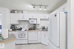 White cabinetry with overhead track lighting, a white electric range, and a white dishwasher - 