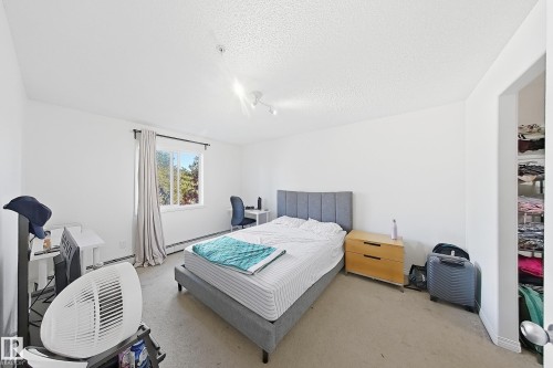 Neutral wall color, carpet flooring, window with curtains, track lighting, and a built-in closet with shelving - #224 3425 19 St Nw, Edmonton, AB 