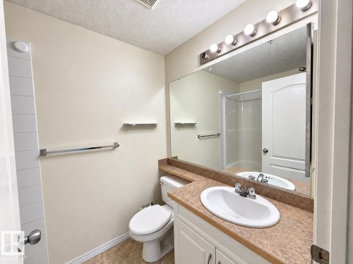 White vanity with a built-in sink, an extended countertop, and an overhead vanity light - #224 3425 19 St Nw, Edmonton, AB 