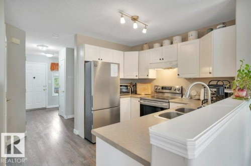 Kitchen featuring white cabinetry, stainless steel appliances, dual basin sink, and a peninsula countertop - 11448 169 Avenue Nw, Edmonton, AB 