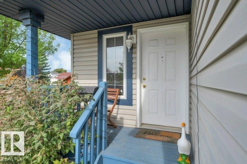 Exterior featuring horizontal siding, a covered porch with blue railings, a multi-pane sidelight, and a paneled entry door - 11448 169 Avenue Nw, Edmonton, AB 