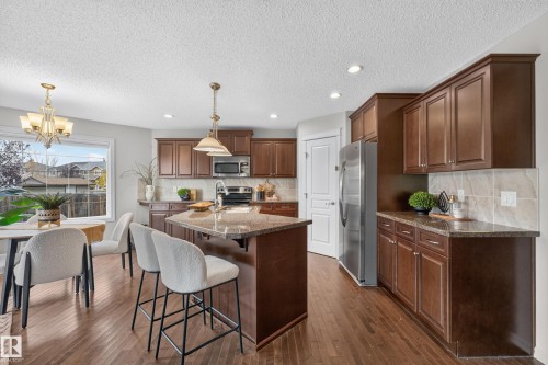 Kitchen featuring dark-toned cabinetry, a central island with stone-finish countertops, stainless steel appliances, wood-finish flooring, and recessed lighting - 7 Bremner, Fort Saskatchewan, AB 
