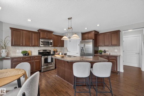 Kitchen featuring dark wood cabinetry, an oversized central island with stone-finish countertops, stainless steel appliances, wood-finish flooring, and recessed lighting - 7 Bremner, Fort Saskatchewan, AB 
