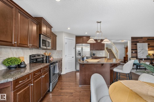 Kitchen featuring dark wood cabinetry, stone-finish countertops, stainless steel appliances, a central island, and wood-finish flooring - 7 Bremner, Fort Saskatchewan, AB 