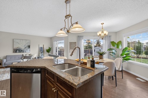 Kitchen island featuring stone countertops, an undermount double-basin stainless steel sink with a high-arch pull-down faucet, and dark-finish cabinetry - 7 Bremner, Fort Saskatchewan, AB 