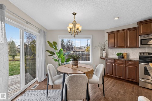 Kitchen featuring dark wood cabinetry, stainless steel appliances, tile backsplash, wood-finish flooring, and sliding glass doors to exterior - 7 Bremner, Fort Saskatchewan, AB 