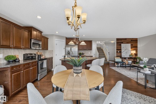 Kitchen featuring rich-toned wood cabinetry, stainless steel appliances, a multi-tiered stone-texture backsplash, and wood-finish flooring, complemented by an accent wall composed of horizontal wood planks - 7 Bremner, Fort Saskatchewan, AB 