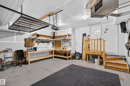 Garage workspace featuring built-in wooden shelving, a fixed workbench, an overhead ceiling-mounted storage rack, and wooden stairs with matching railing - 7 Bremner, Fort Saskatchewan, AB 