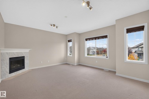 Neutral-toned interior space featuring a fireplace with a stone-finish surround, multi-pane windows with integrated blinds, and track lighting fixtures - 7 Bremner, Fort Saskatchewan, AB 
