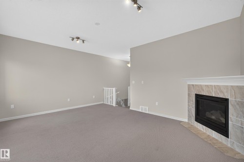 Fireplace featuring a stone-tile surround, neutral carpeting, and adjustable multi-light track fixtures - 7 Bremner, Fort Saskatchewan, AB 