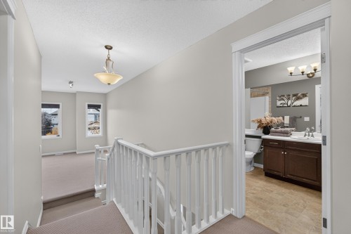 Neutral-toned interior featuring wall-to-wall carpeting, white spindle railing, multi-pane windows, and a bathroom equipped with dark-finish wood cabinetry and a tiled floor - 7 Bremner, Fort Saskatchewan, AB 