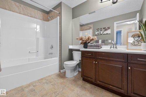 Bathroom featuring a white tub-shower combination with surround tiling, a dark wood vanity, a surface-mounted sink, a wide wall-mounted mirror, and tile-finish flooring - 7 Bremner, Fort Saskatchewan, AB 
