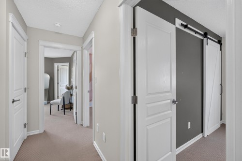 Interior hallway featuring crisp white trim, three-panel interior doors, carpeted flooring, and a white sliding barn door with matte black hardware mounted on a charcoal-painted accent wall - 7 Bremner, Fort Saskatchewan, AB 