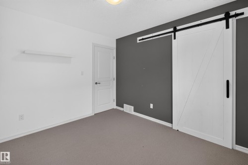 Room featuring a sliding barn-style door with matte black hardware, a contrasting accent wall, a six-panel door, and a wall-mounted floating shelf - 7 Bremner, Fort Saskatchewan, AB 