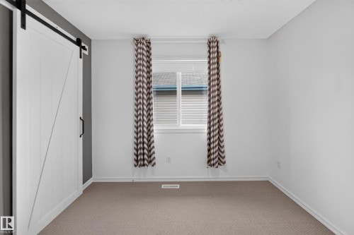 White sliding barn door with matte black hardware, neutral-toned wall-to-wall carpeting, and a dual-pane window - 7 Bremner, Fort Saskatchewan, AB 