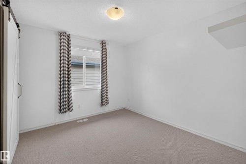 Room featuring neutral carpeting, a sliding barn-style door, single-window fenestration, and a ceiling-mounted light fixture - 7 Bremner, Fort Saskatchewan, AB 