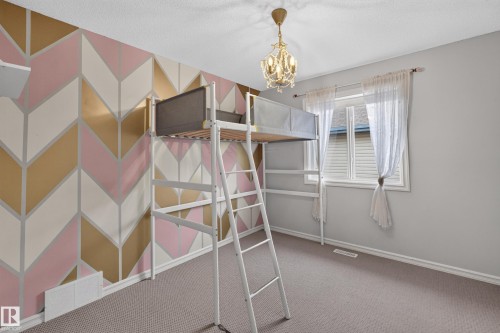 Bedroom featuring a geometric-patterned accent wall, neutral carpeting, and a multi-tiered crystal-style chandelier - 7 Bremner, Fort Saskatchewan, AB 