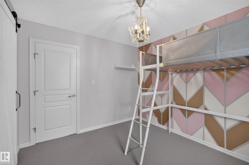 Geometric patterned accent wall, neutral carpeting, sliding door with matte black hardware, and ornate chandelier fixture - 7 Bremner, Fort Saskatchewan, AB 