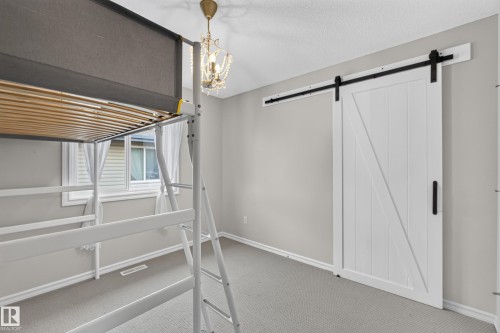 Room featuring a white sliding barn door with matte black hardware, wall-to-wall carpeting, and a crystal-accented chandelier fixture - 7 Bremner, Fort Saskatchewan, AB 