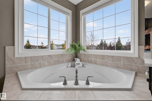 Corner soaking tub featuring a white acrylic finish, chrome deck-mounted faucet, and natural stone-finish tile surround - 7 Bremner, Fort Saskatchewan, AB 