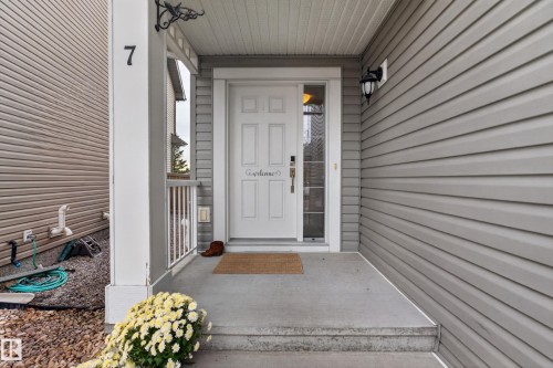 Covered entryway featuring horizontal vinyl siding, a six-panel front door with a vertical glass sidelight, and an attached wall-mounted lantern fixture - 7 Bremner, Fort Saskatchewan, AB 